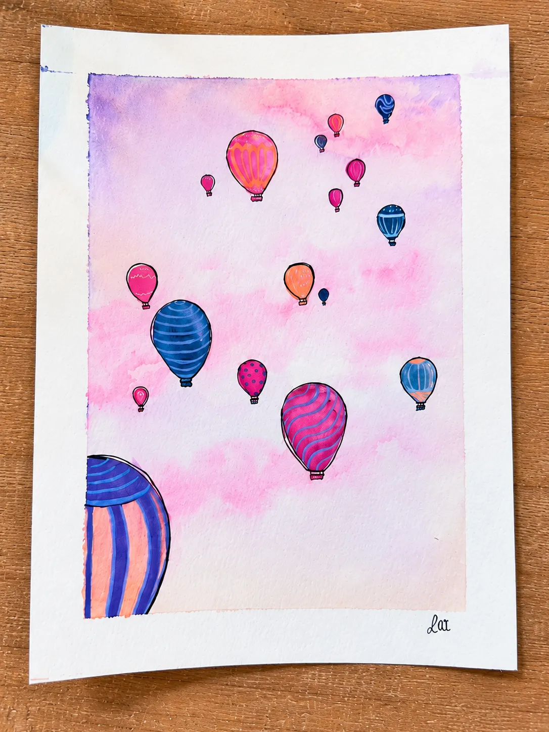 Hot air balloon watercolor viewed from overhead beside green leaves