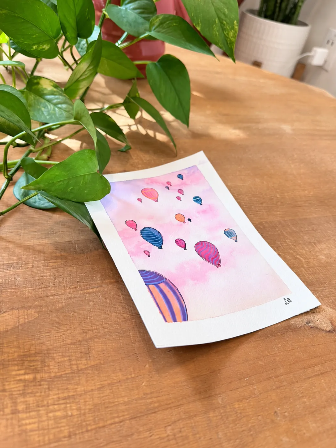 Hot air balloon watercolor viewed at an angle beside a trailing plant