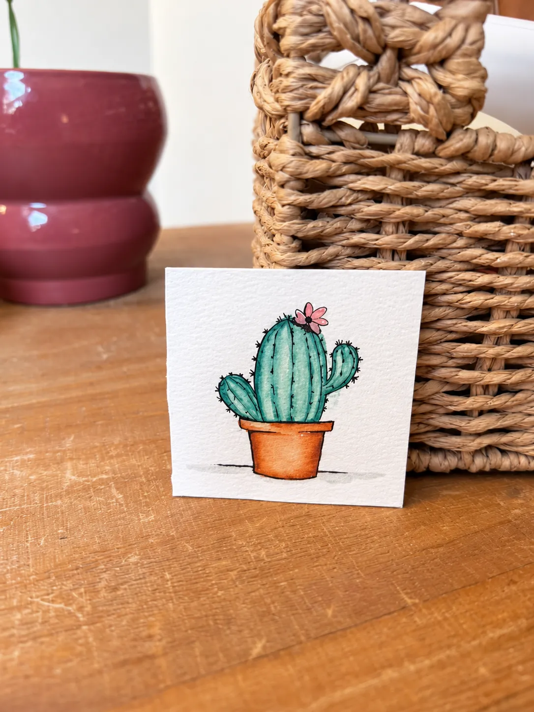 Little Bloom standing on a wooden table against a woven basket