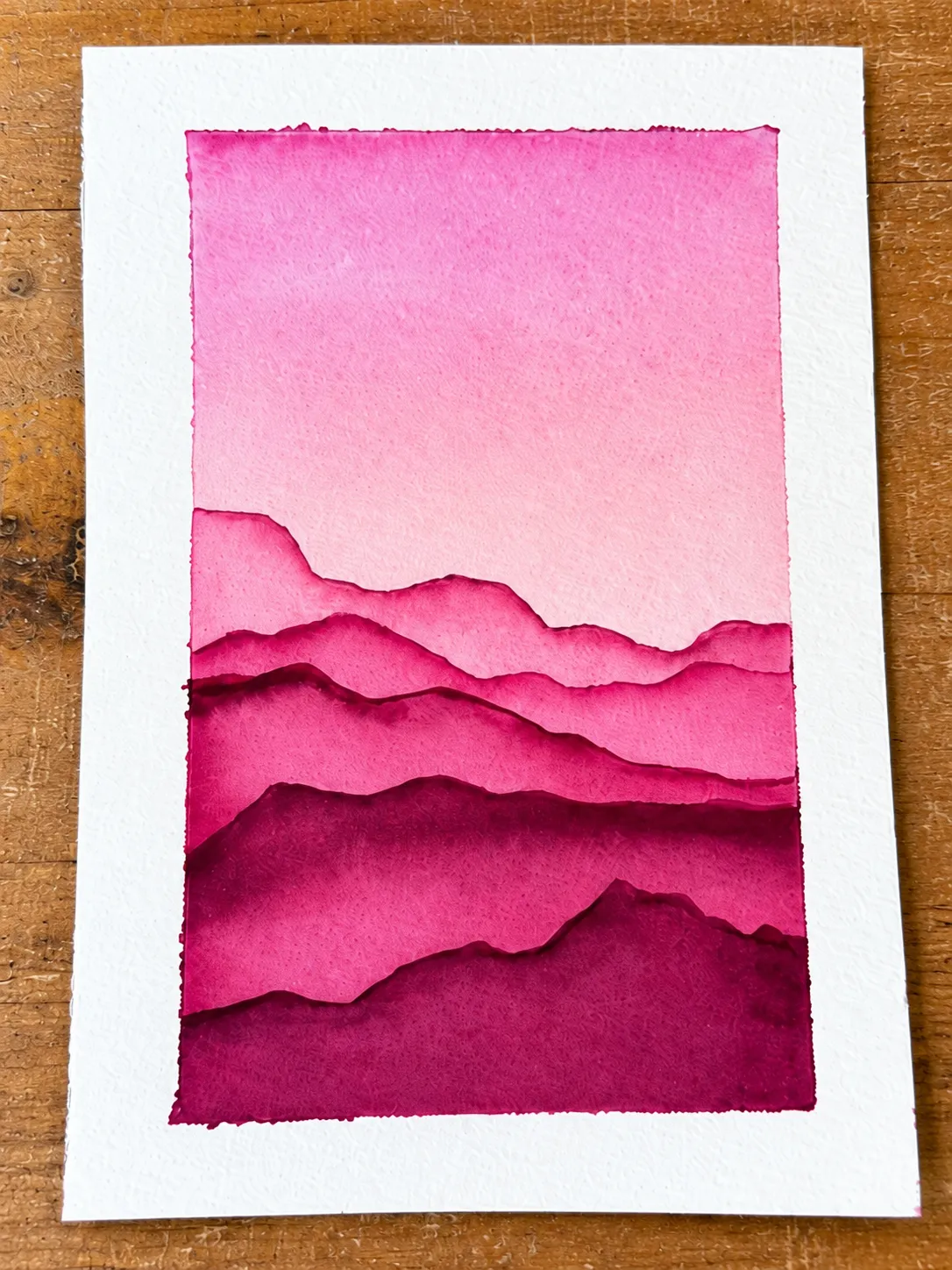 Layered pink mountain watercolor lying on a wooden table