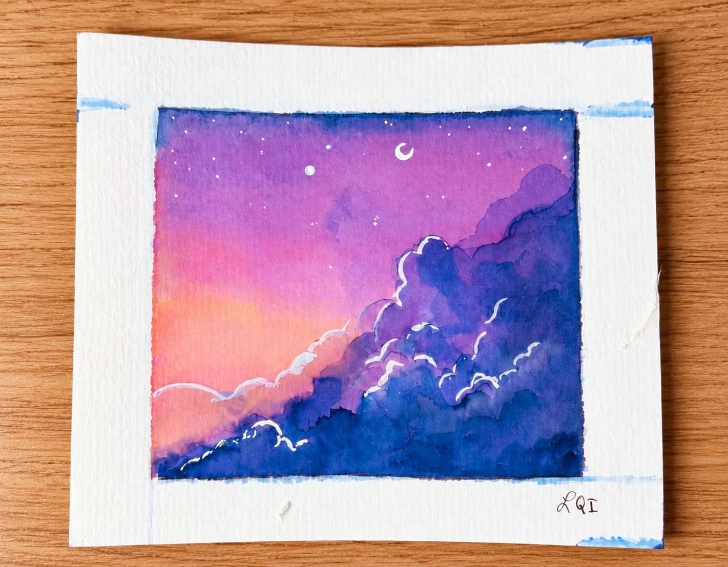 Purple clouds beneath a crescent moon watercolor on a wooden table